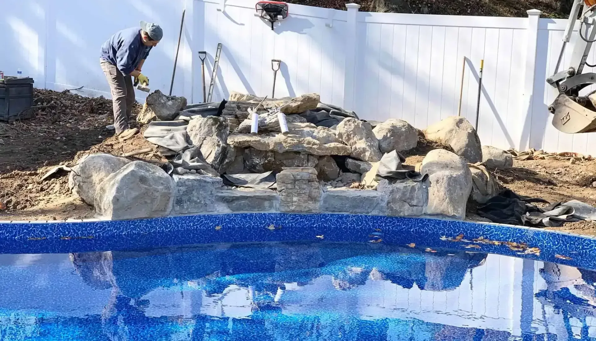Outdoor Swimming Pool | Libardi Island Landscaping Corp. A man is working on a swimming pool next to a white fence.