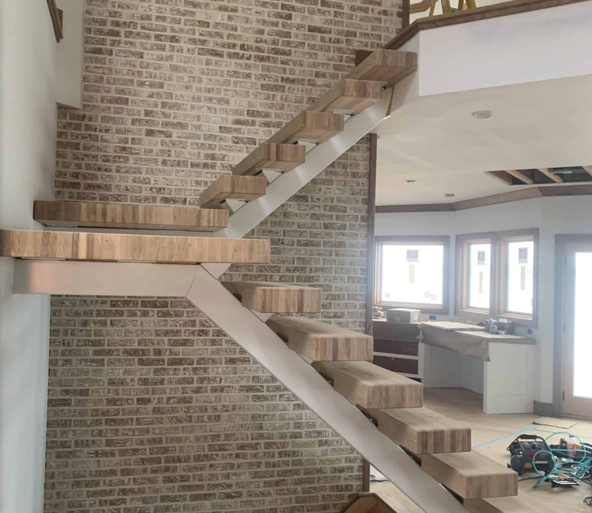 A wooden staircase with a white railing in front of a brick wall