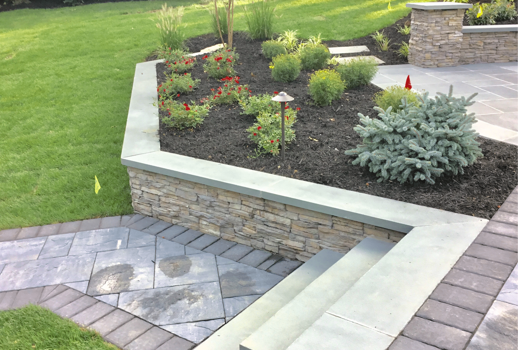 A garden with a stone wall and a brick walkway