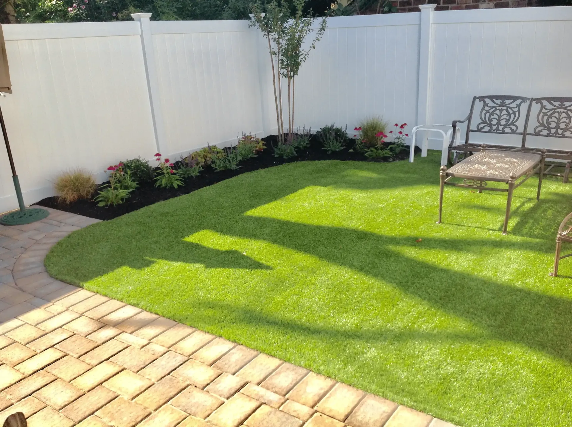 A backyard with a brick patio and a bench and chairs.