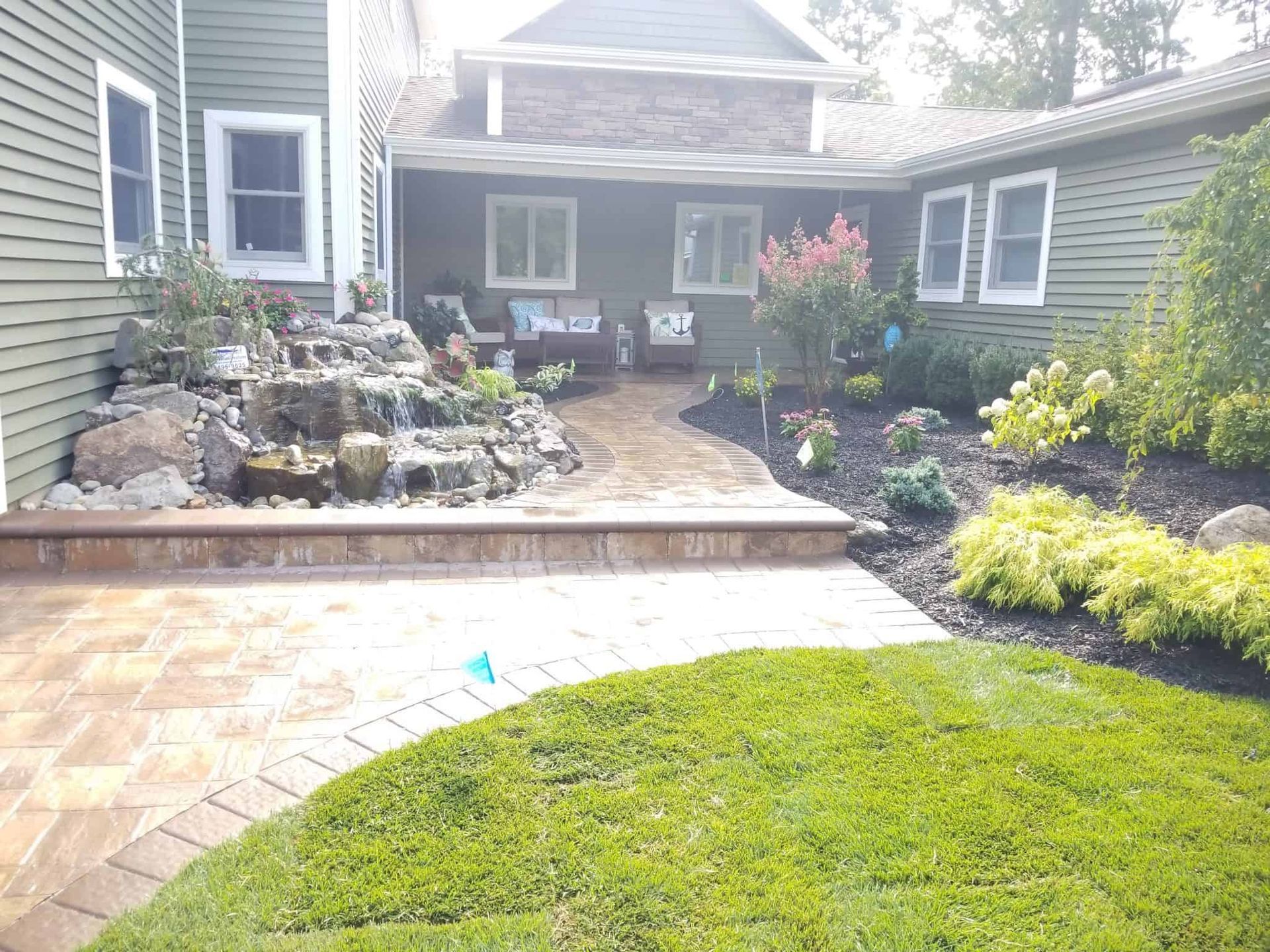 A brick walkway leading to a house with a waterfall in the backyard.