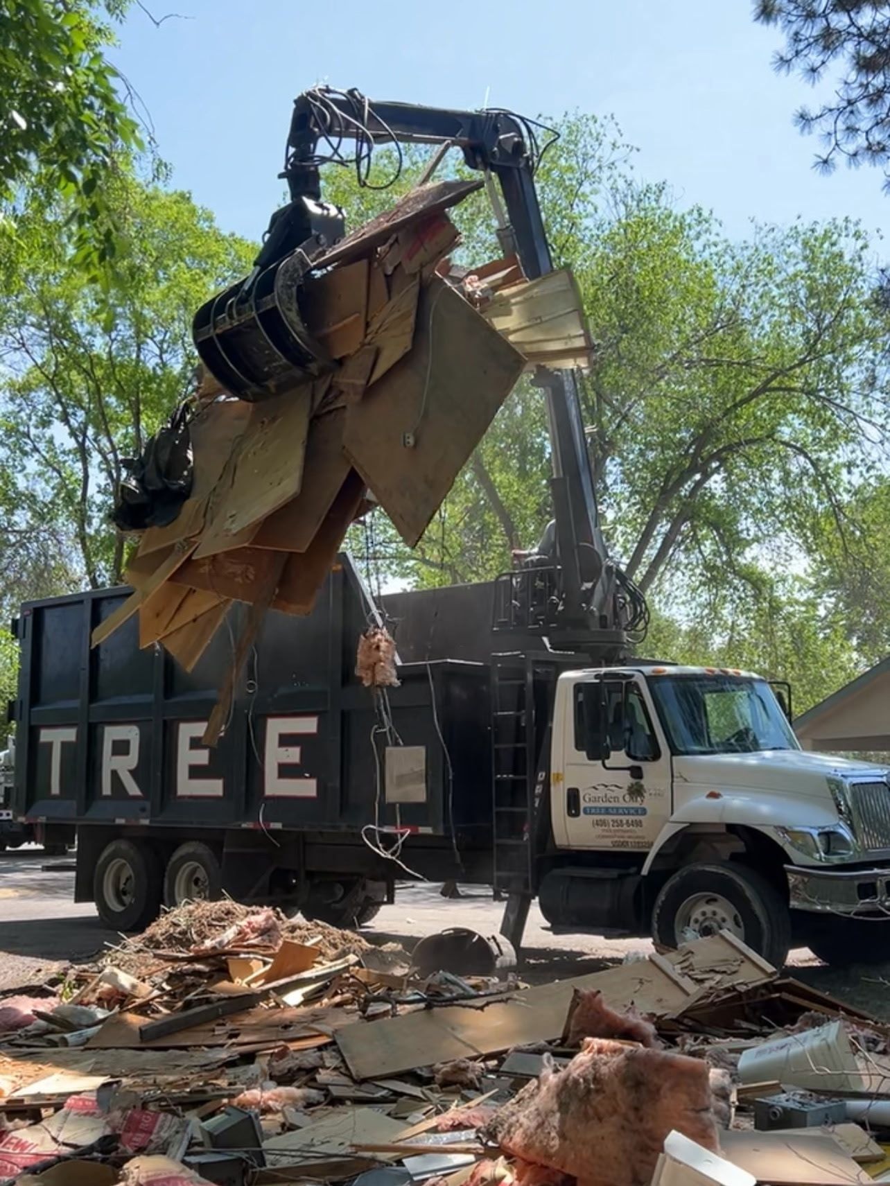 A truck with a crane-like arm loads debris from a construction site. The truck is labeled