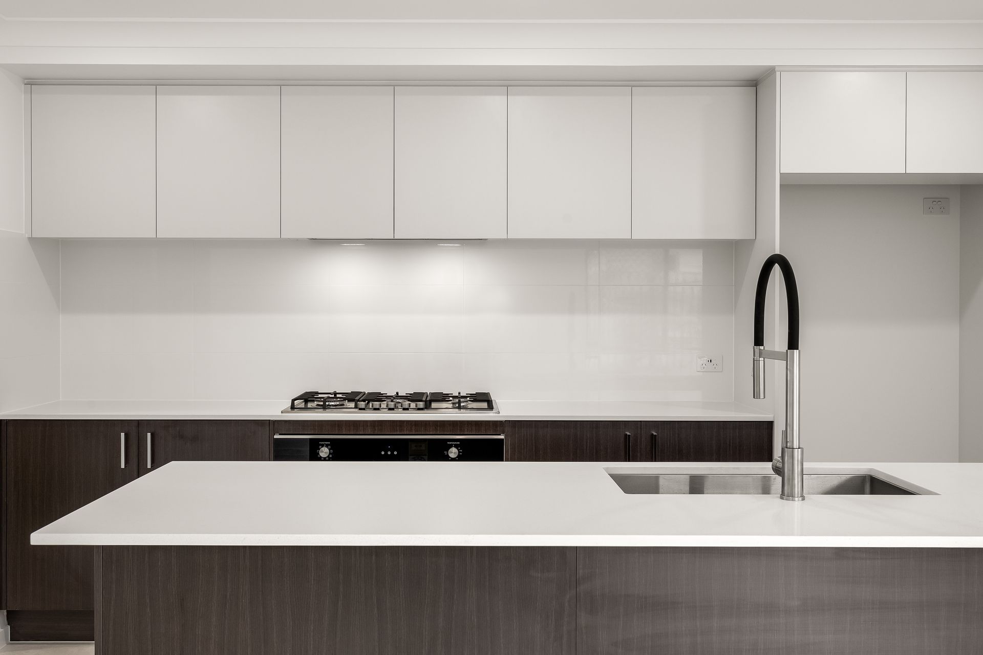Modern kitchen with white and dark brown cabinets, island with sink, and gas cooktop.