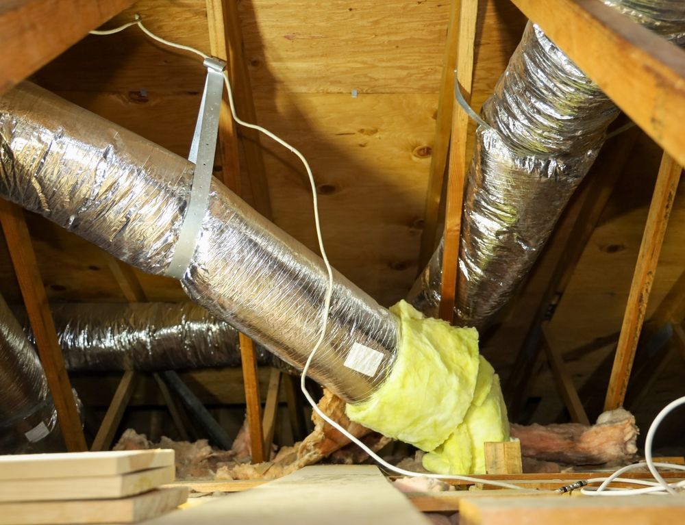 Insulated flexible HVAC ducts suspended by metal straps in a wooden attic space.