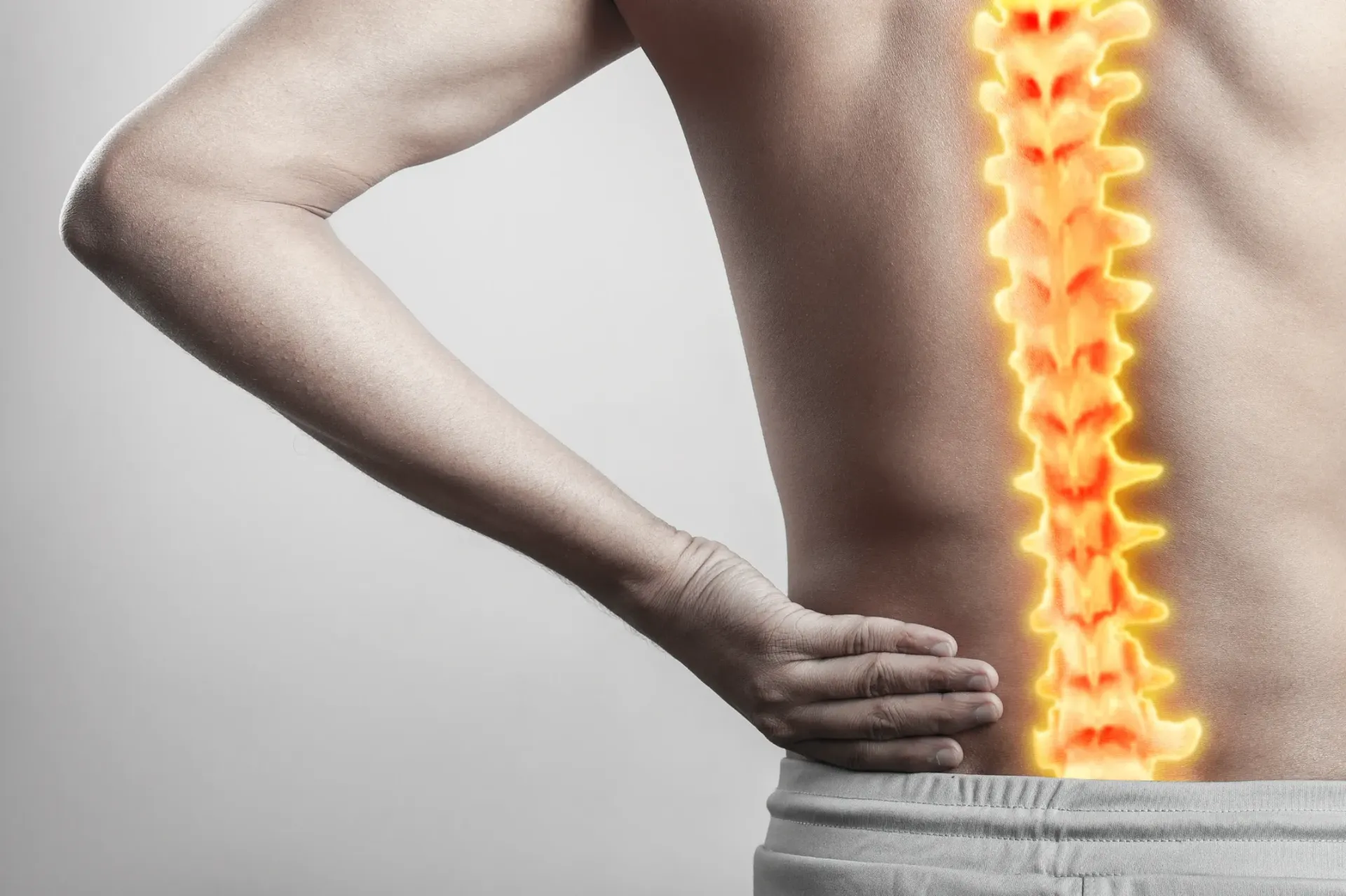 Man with hand on lower back, spine highlighted in orange, showing pain. — Bourbong Street Physiotherapy Centre in Bundaberg West, QLD