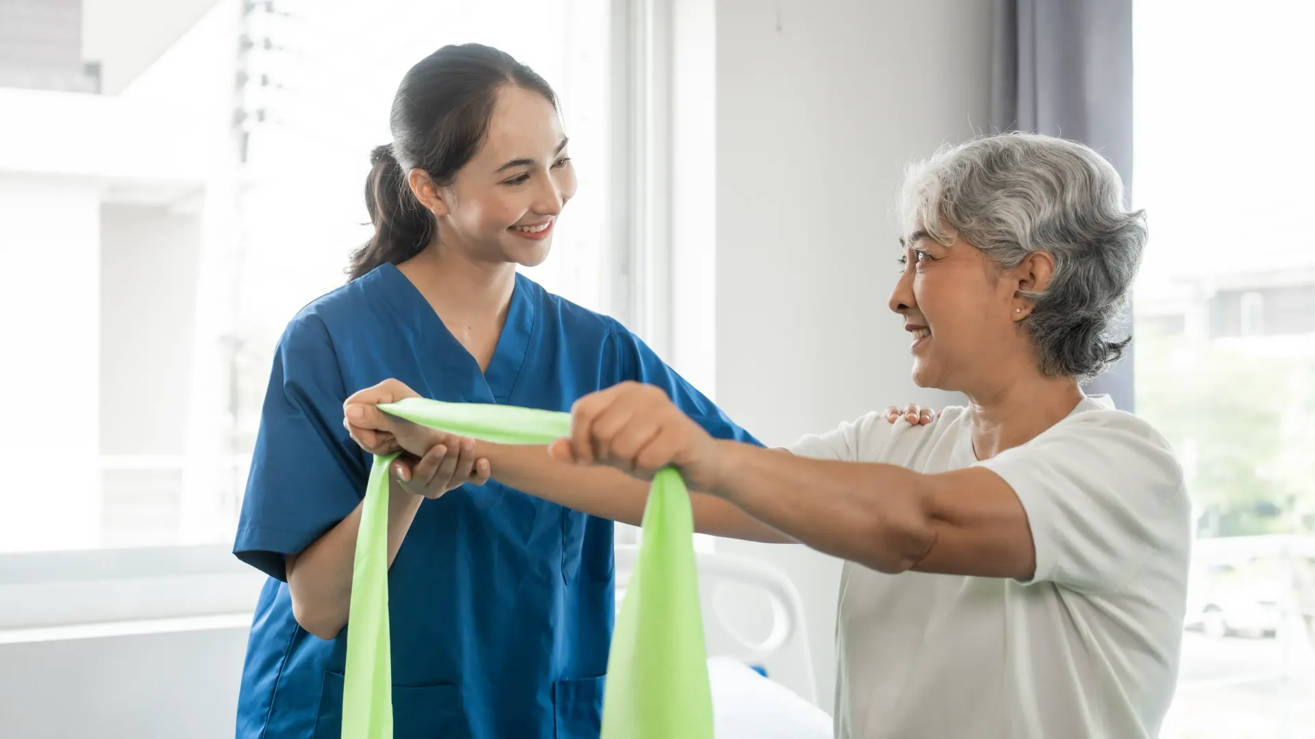 Therapist assists a patient using resistance band for arm exercise. Both are smiling. — Bourbong Street Physiotherapy Centre in Bundaberg West, QLD
