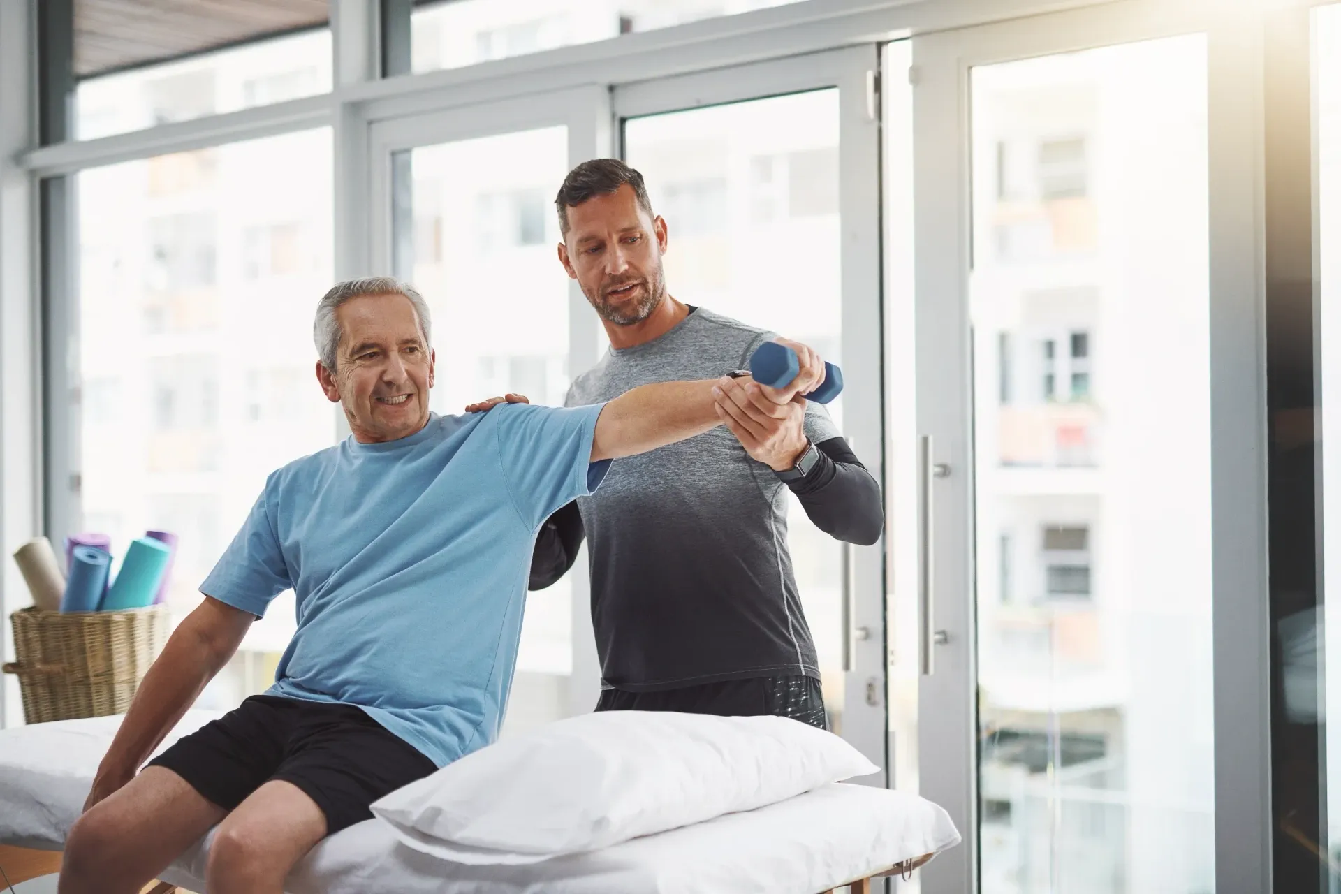 Therapist assisting a person lifting a small dumbbell; indoor setting with bright light. — Bourbong Street Physiotherapy Centre in Bundaberg West, QLD