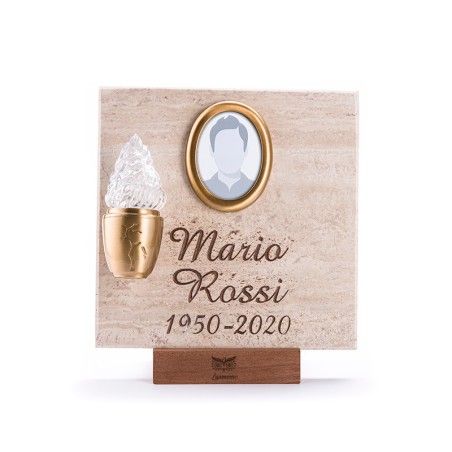 Una targa commemorativa quadrata in pietra con una cornice ovale dorata per foto, una fiamma di vetro annessa e la scritta