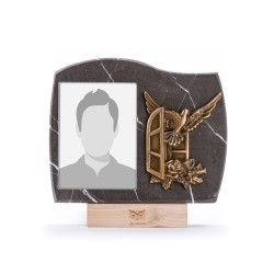 Una targa commemorativa rettangolare in marmo scuro con cornice portafoto, scultura di una colomba in bronzo e base in legno.
