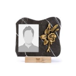 Una targa commemorativa in marmo nero con una cornice portafoto e una rosa decorativa in metallo dorato, posta su una base di legno.