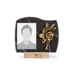 Una cornice commemorativa in marmo nero con uno spazio per il ritratto e una rosa decorativa in bronzo, poggiata su una base di legno.