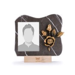Una cornice commemorativa con sfondo in marmo nero e una scultura di rosa in bronzo, montata su una base in legno chiaro.