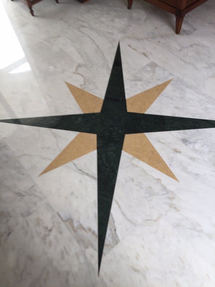 Un intarsio sul pavimento raffigurante una stella a quattro punte verde scuro sovrapposta a una stella a quattro punte più grande, color beige chiaro, su marmo.