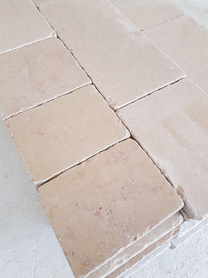 Una ripresa ravvicinata e dall'alto di una pila di piastrelle o lastre di pietra quadrate, di colore beige chiaro, con una finitura opaca e ruvida.