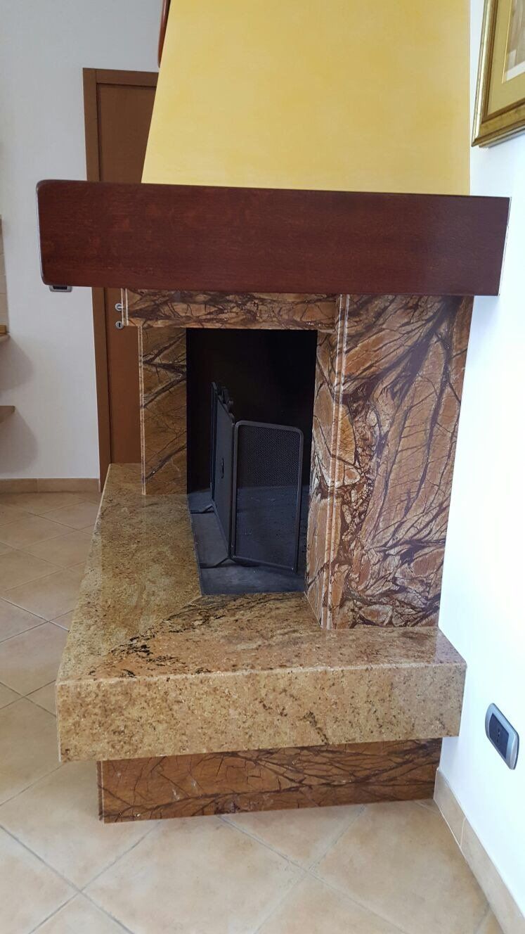 Un camino caratterizzato da una mensola marrone scuro, una cornice in pietra marrone con superficie ruvida e un focolare in pietra dorata screziata.