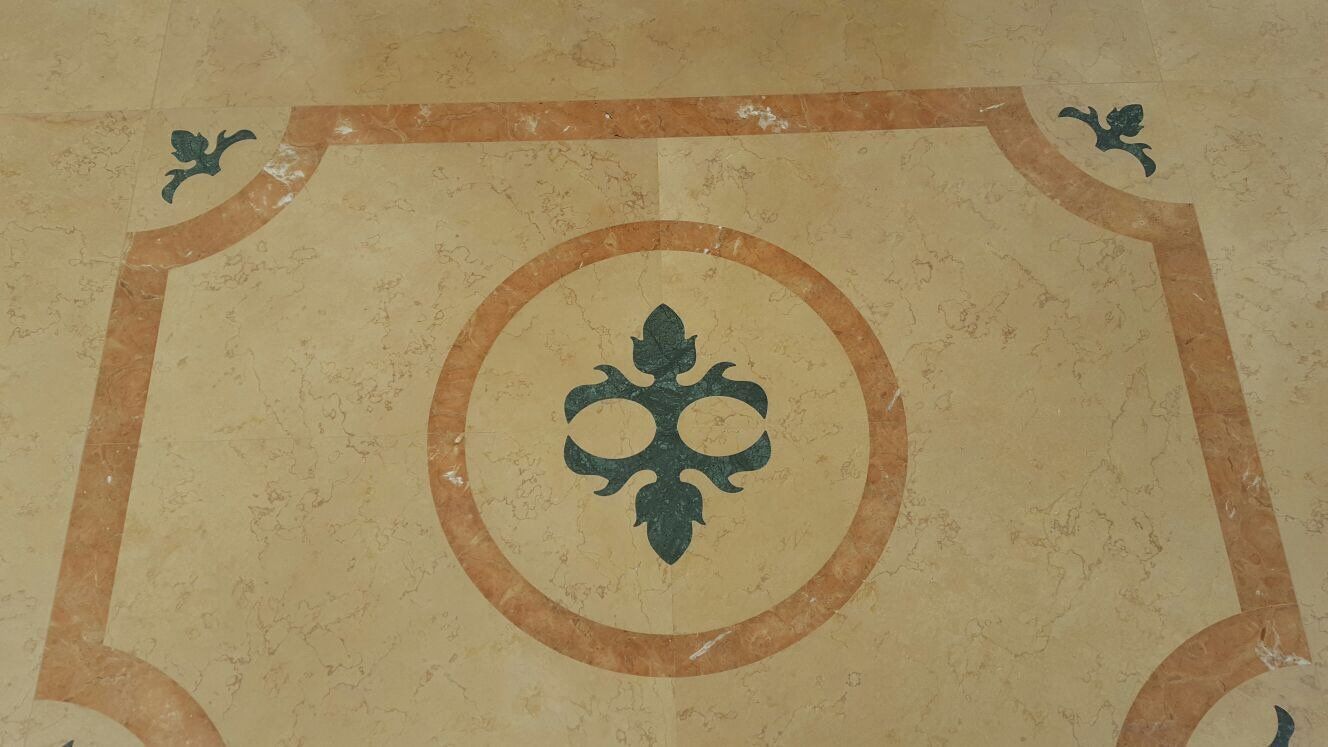 Un pavimento in pietra color crema con un intarsio floreale verde scuro al centro di un anello e un bordo decorativo esterno.
