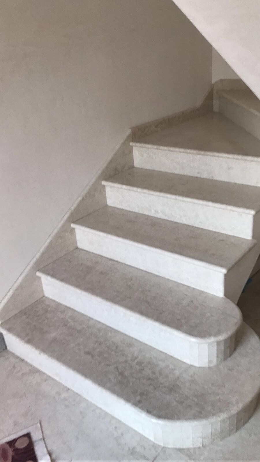 Una scalinata in pietra che sale verso l'alto, con un gradino inferiore curvo, stagliata contro una semplice parete bianca.