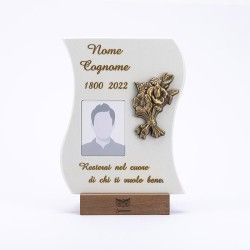 Una targa commemorativa con nome e date provvisori, una cornice per il ritratto, un emblema floreale in bronzo e testo in italiano.