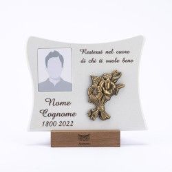 Una targa commemorativa bianca e curva su una base di legno, con cornice portafoto, ornamento floreale in ottone e spazi per il testo.