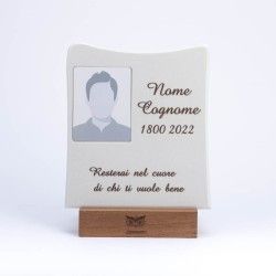 Una targa commemorativa in pietra con una cornice portafoto, nome, date e un'iscrizione sentita, poggiata su una base di legno.