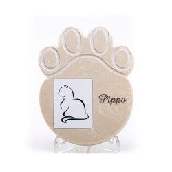 Una targa commemorativa per animali domestici di colore beige, a forma di zampa, su un supporto, con la silhouette di un gatto e il nome inciso