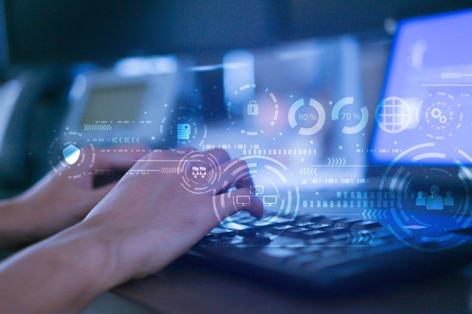 Mani che digitano su un computer portatile con sovrapposizione di dati digitali; tonalità blu, ambiente interno.