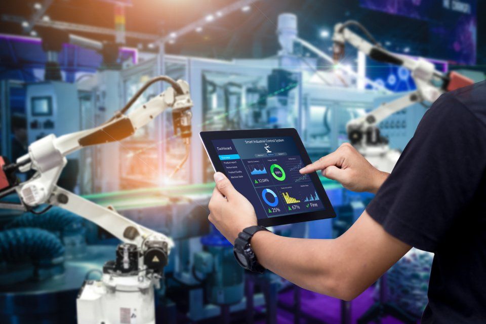 Uomo che usa un tablet in fabbrica, controllando bracci robotici e monitorando i dati.