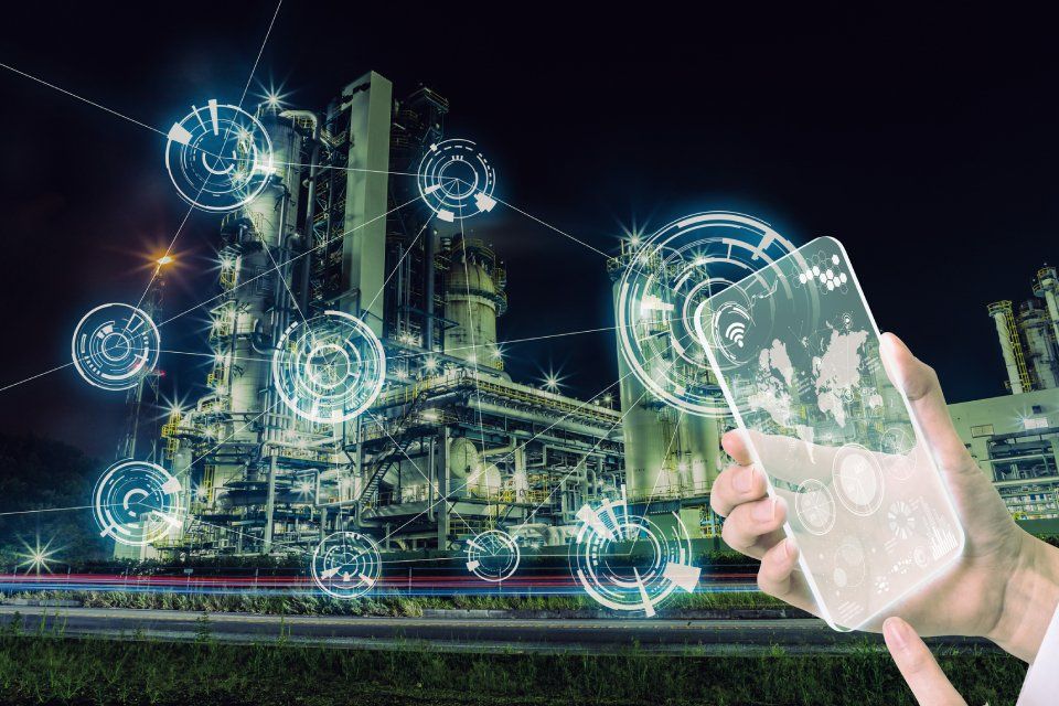 Una persona con in mano un telefono visualizza i dati su uno stabilimento industriale di notte.