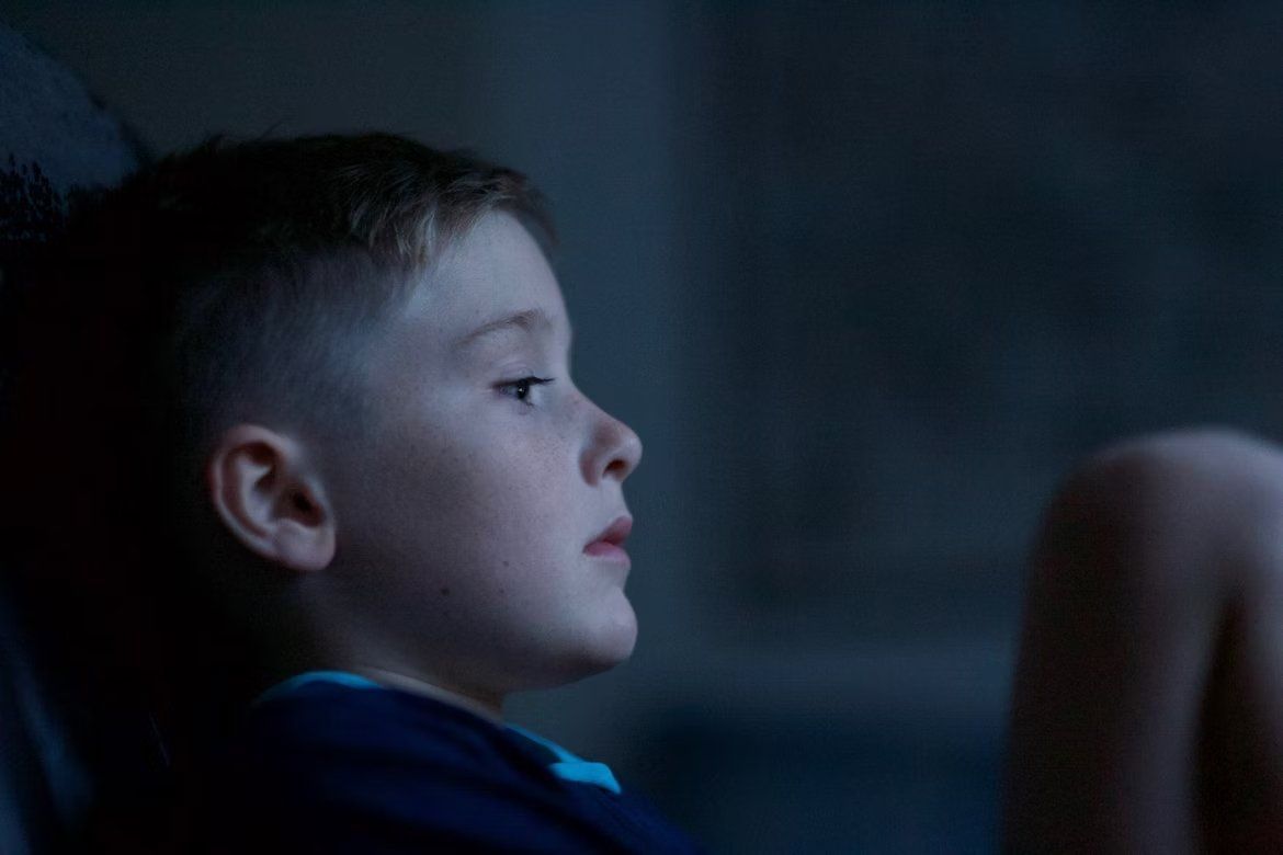 Side profile of a child watching intently in a dim blue-lit room