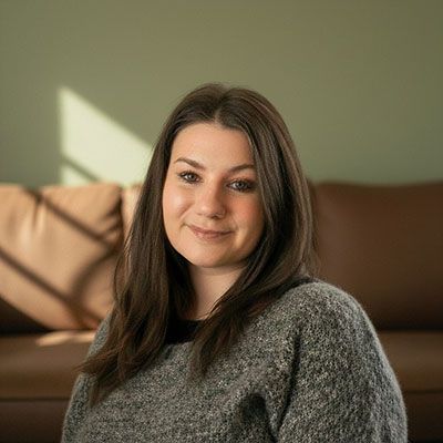 Woman smiling on a couch in warm sunlight, wearing a gray sweater.