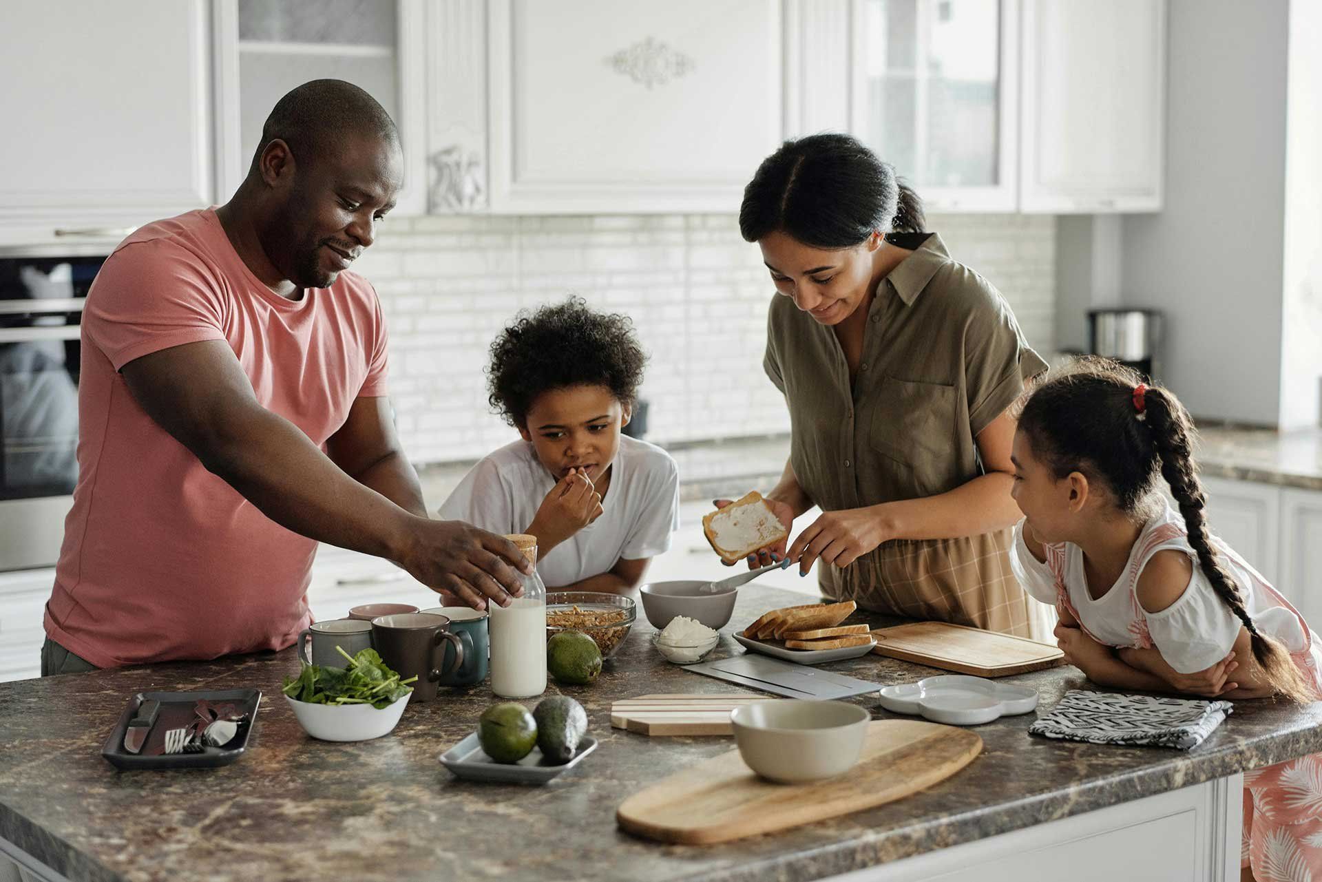 Family preparing food together in a bright kitchen around a counter with bowls, vegetables, and a cutting board