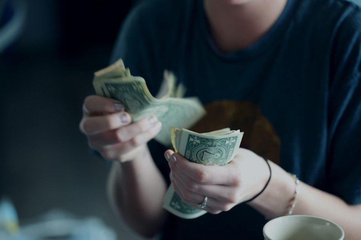 Hands counting stacks of cash at a table in dim light