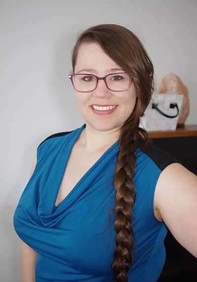 Person in a blue top and glasses with a long braid, smiling indoors.