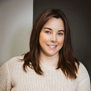 Smiling woman in a cream sweater against a neutral gray background