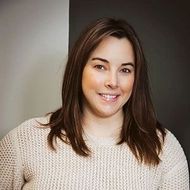 Smiling woman in a cream sweater against a neutral gray background
