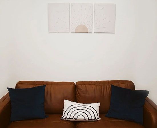 Brown leather sofa with navy and white pillows beneath a minimalist wall artwork