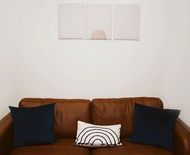 Brown leather sofa with navy and white pillows beneath a minimalist wall artwork