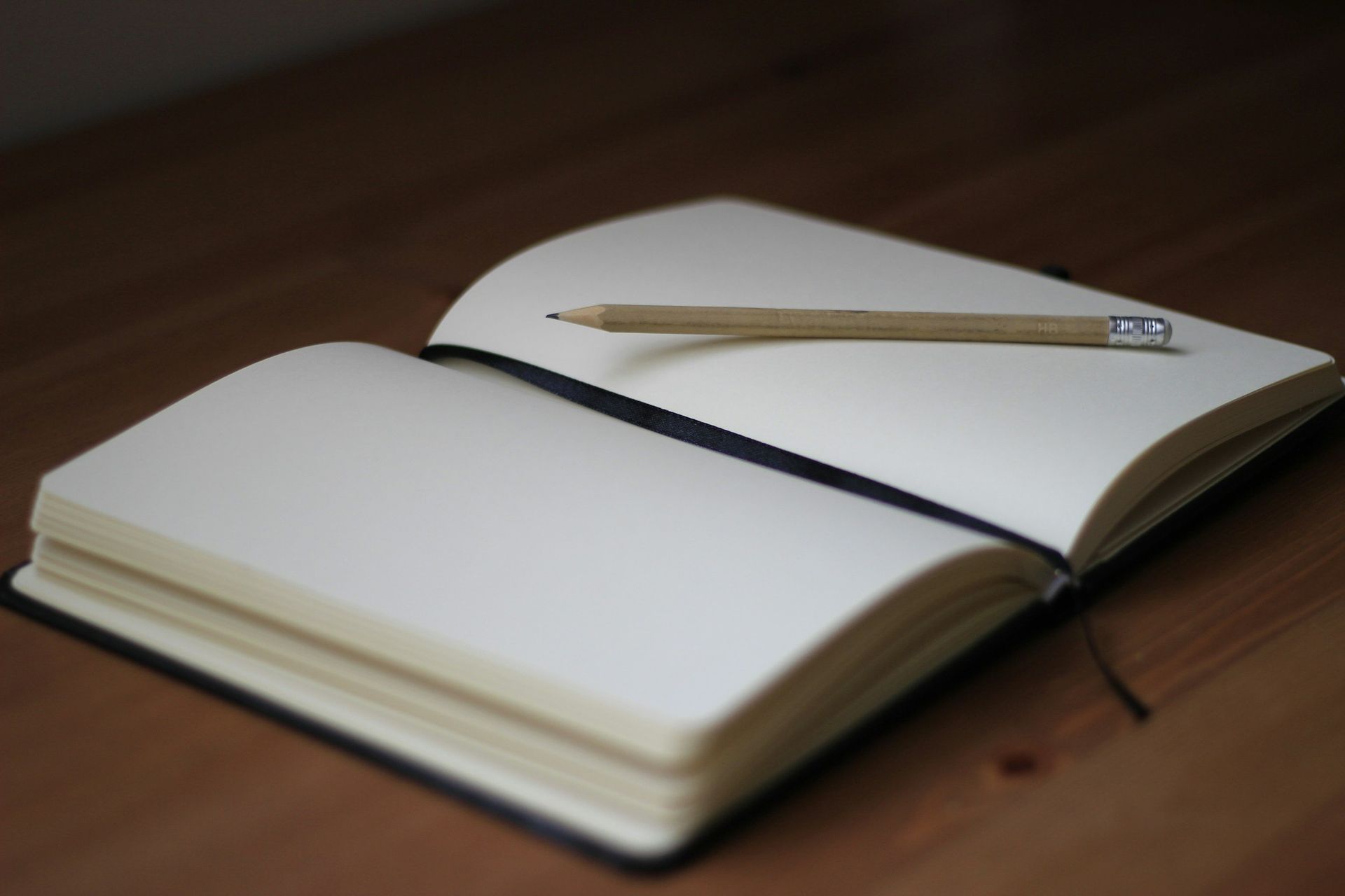 Open notebook with a pencil resting on it on a wooden table
