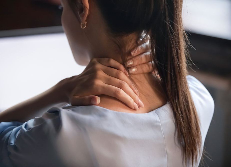 A woman is holding her neck in pain while sitting in front of a computer.