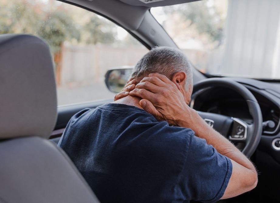 A man is sitting in a car with his hands on his neck.
