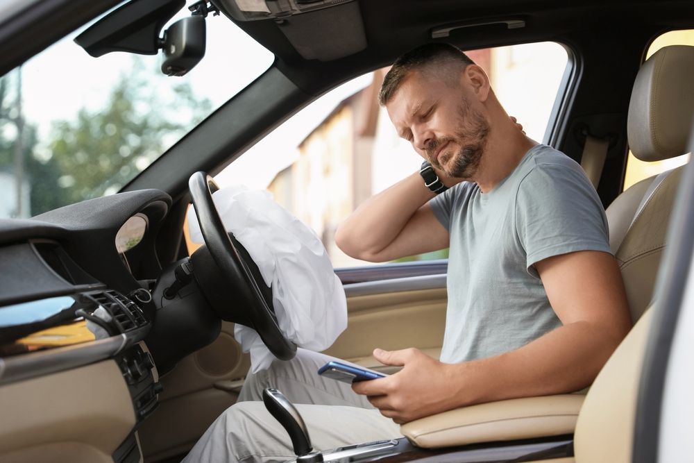 A man is sitting in a car with an airbag on the steering wheel.