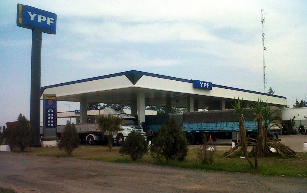 Gasolinera YPF con marquesina blanca y letrero azul, vista junto a una carretera bajo un cielo nublado.