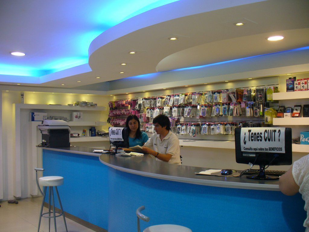 Barra de color azul brillante con dos empleados en una cafetería o salón moderno, con estantes de bebidas detrás de ellos.
