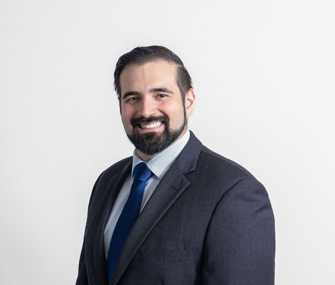A man with a beard is wearing a suit and tie and smiling.