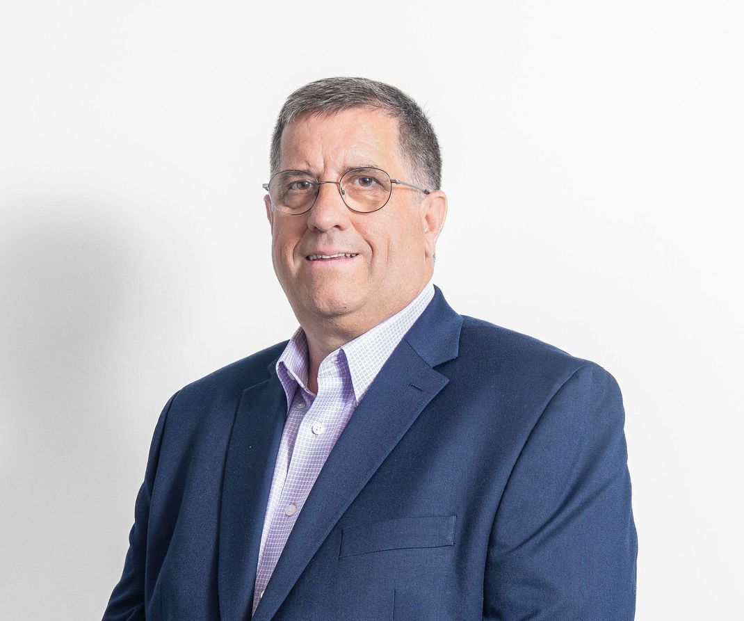 A man in a blue suit and glasses is smiling for the camera.