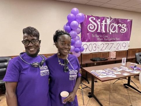 Two women in purple shirts stand by a