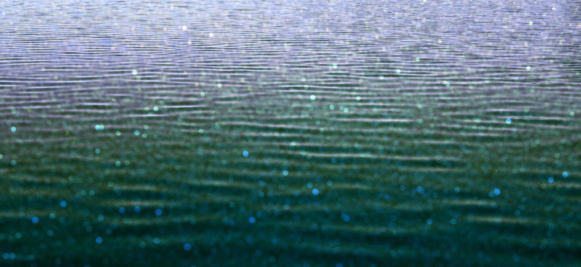 A close up of a body of water with waves and rain drops on it.