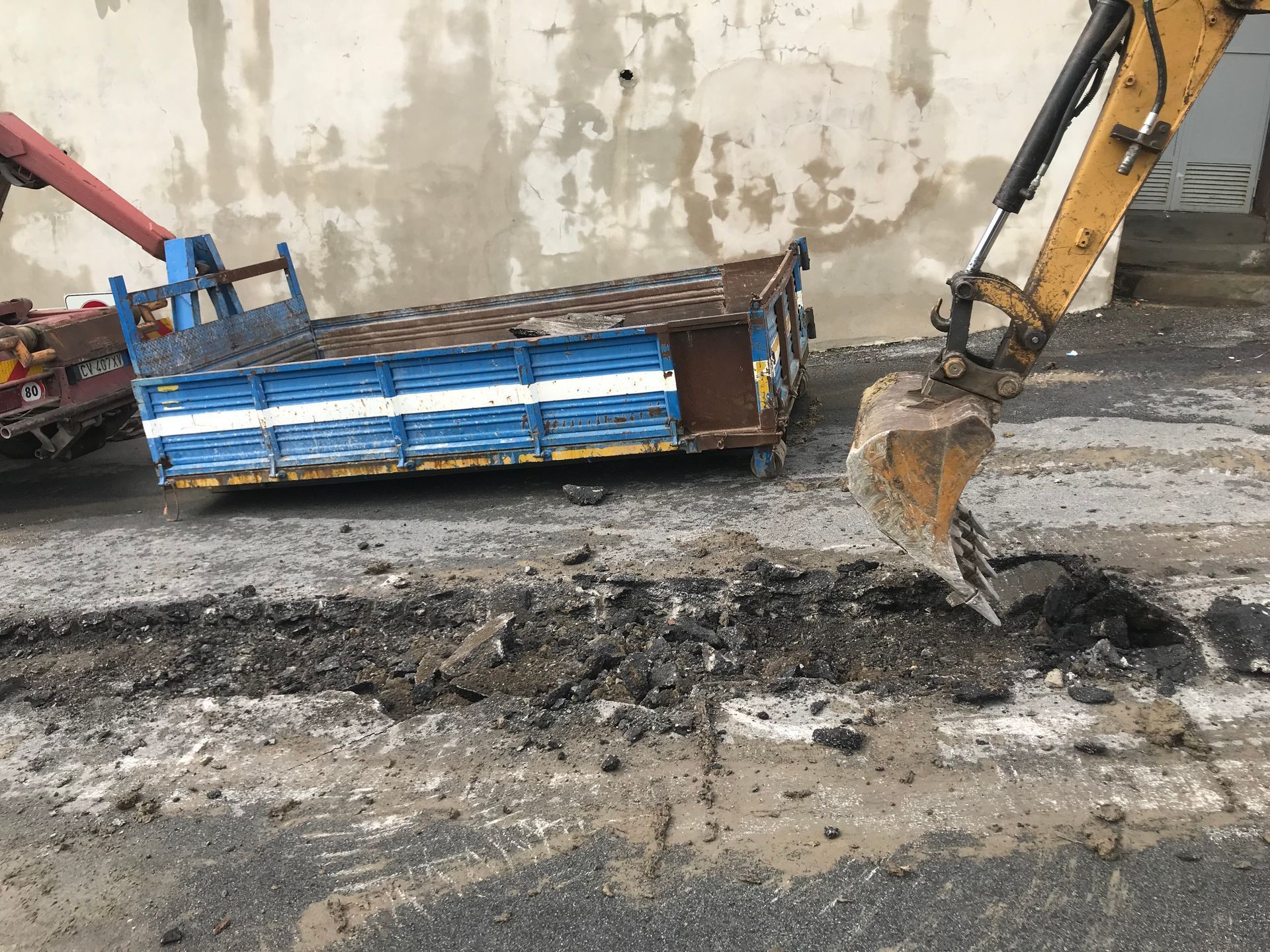 Un escavatore giallo sta scavando una buca nel terreno accanto a un camion blu.