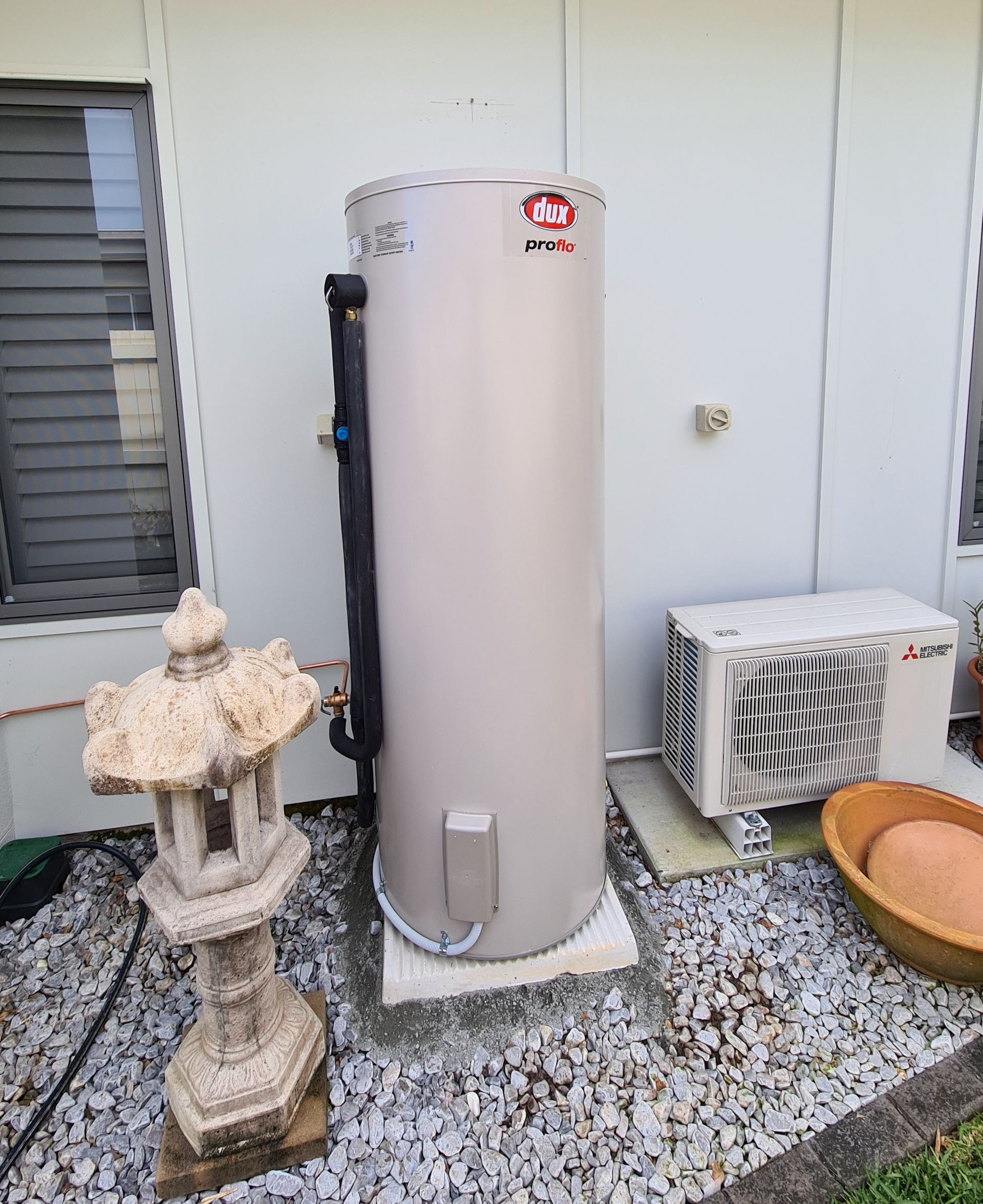 A Tall, White Hot Water Heater Tank in a Dimly Lit, Unfinished Basement Setting — 24/7 Hot Water in Valdora, QLD