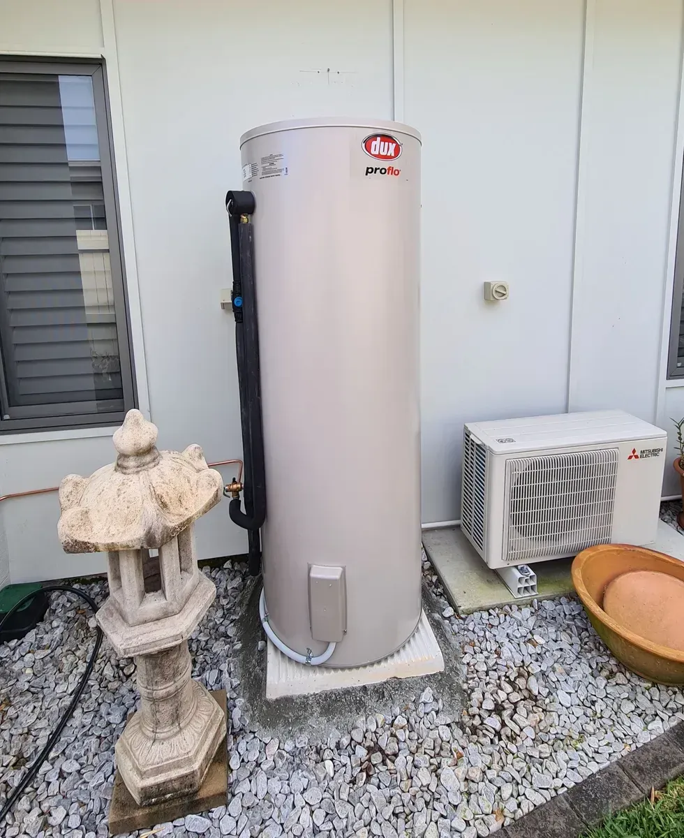 A Cylindrical Water Heater Outside, Next to an Air Conditioning Unit and a Stone Lantern — 24/7 Hot Water in Valdora, QLD